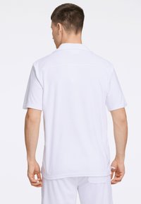 Witte polo in zacht, badstof met korte mouwen en een kraag. Heeft een relaxte pasvorm en subtiele stikseldetails.