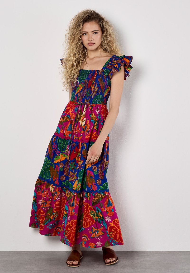 Robe maxi multicolore avec des motifs floraux et de feuilles. Présente des bretelles froncées, un corsage smocké et une jupe à volants. Sandales plates.
