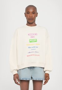 Krémová mikina s multicolornými textovými logami "MOSCHINO JEANS" v rôznych písmach. Dizajn má spadnuté ramenné švy a rebrované lemy.