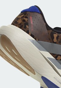 Gros plan du talon d'une chaussure de course à imprimé léopard avec semelle blanche, languette de talon bleue, bandes grises et texte « ADIZERO EVO SL ».