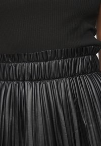 Schwarzes, geripptes Top mit einem plissierten Rock aus Kunstleder, ausgestattet mit einem elastischen Taillenbund und einem glänzenden, strukturierten Finish.