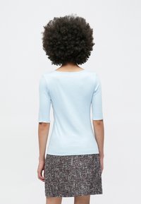 Lichtblauw nauwsluitend shirt met driekwartmouwen en een brede halslijn, gecombineerd met een gestructureerde, meerkleurige rok.