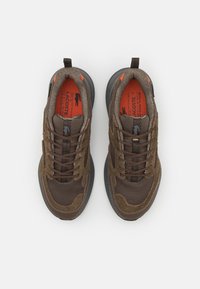 Brown athletic shoes with mesh and suede material, featuring a textured surface, brown laces, and orange inner lining. Black logo accents.