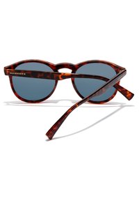 Kulate brýle s plastovým rámečkem v barvě želvoviny a tmavě šedými skly. Na spáncích mají zlaté logo "HAWKERS".