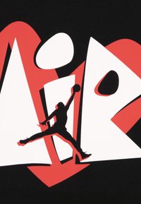 Μαύρο ύφασμα με έντονο λευκό και κόκκινο γραφιστικό σχέδιο, που περιλαμβάνει τα γράμματα «AIR» και τη σιλουέτα ενός πηδώντας φιγούρας που κρατάει ένα μπάσκετ.