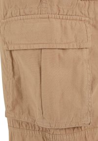 Beige cargo shorts feature a flap pocket with stitched edges and a textured fabric. The fabric is soft and lightweight, ideal for warm weather.