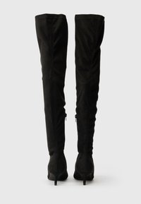 Mustad üle põlve saapad pehmest sametist, millel on sujuv, vormitud disain, terav nina ja õhukesed kõrged kontsad külgkettidega.