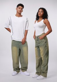 Hvit oversized T-skjorte med svart stripe-detalle, kombinert med lysegrønne baggy jeans. Begge har på seg hvite sneakers, som viser en avslappet stil.