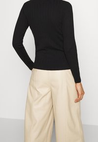 Schwarzer gerippter Strickpullover mit langen Ärmeln, tailliert. Kombiniert mit weiten beigen Hosen, die eine glatte Stoffstruktur zeigen.