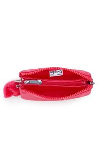 Portafoglio rosso con zip realizzato in materiale liscio, caratterizzato da un dettaglio in pom-pon peloso. L'interno include tasche e un'etichetta brandizzata.