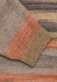 Striktrøje lavet af stof med orange, beige og grå striber. Har en ribkant i levende farver, der fremhæver de forskellige teksturer.