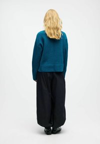 Turkusowy sweter z wełny w kroju cropped, zestawiony z luźnymi czarnymi spodniami i błyszczącymi czarnymi butami, widok z tyłu.