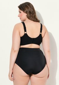 Zwarte kant bralette met verstelbare bandjes en haak-en-oogsluitingen, gecombineerd met zwarte high-waisted onderkleding. Gladde textuur met subtiele patronen.