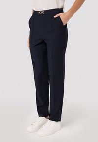 Marineblauwe tailored broeken met een gladde textuur, voorzien van een gouden gespsluiting, twee zijzakken en een recht model. Draag ze met witte sneakers.