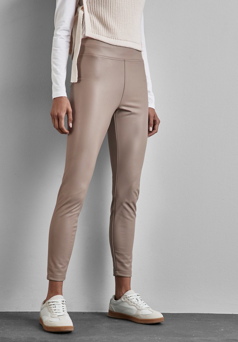 Strakke, beige leggings van leerachtige stof, met een gladde textuur en een hoge tailleband, gecombineerd met witte sneakers.