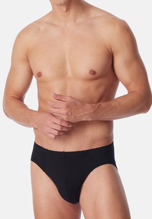 Schwarze Baumwollslips mit glatter Textur, im klassischen Slip-Schnitt und elastischem Bund, getragen von einem männlichen Model mit freiem Oberkörper.