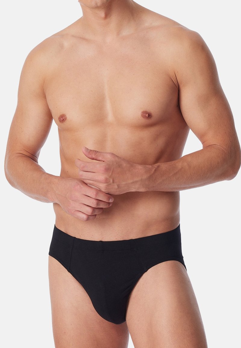 Slip neri in cotone con una texture liscia, caratterizzati da un taglio classico e una cintura elastica, indossati da un modello maschile con il torso scoperto.
