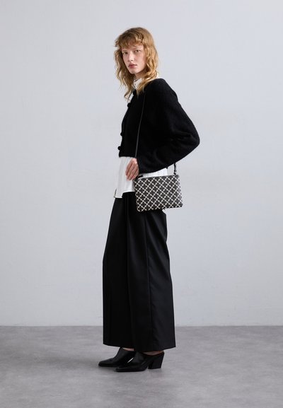 Maglione corto nero con tessuto testurizzato, camicia bianca sotto, pantaloni neri a gamba larga, scarpe col tacco nere e una borsa a fantasia.