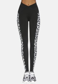 Czarne legginsy z białymi paskami w panterkę po bokach, z wysokim stanem i gładkim, elastycznym materiałem. Dopasowane do butów sportowych w zwierzęcy wzór.