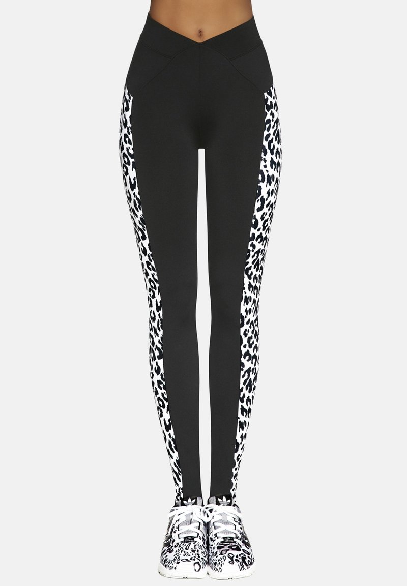 Czarne legginsy z białymi paskami w panterkę po bokach, z wysokim stanem i gładkim, elastycznym materiałem. Dopasowane do butów sportowych w zwierzęcy wzór.