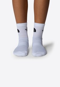 Calcetines blancos de corte de tripulación con borde acanalado, que presentan acentos de logo negro y un diseño de punto texturizado, mostrados sobre pies descalzos.