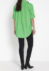 Grön kortärmad skjorta med mittfalldetalj och böjd nederkant, matchad med svarta skinny jeans och svarta klackiga ankelskor.