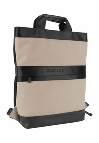 Beige und schwarze Rucksack aus glattem Material; verfügt über ein Logo, zwei obere Griffe, seitliche Netztaschen und verstellbare Riemen.