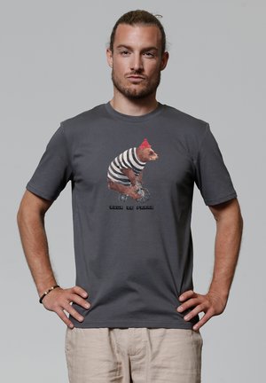 Graues Baumwoll-T-Shirt mit kurzen Ärmeln, das eine Bärenillustration in einem gestreiften Hemd und rotem Hut zeigt. Der Text unter dem Design lautet "pour Le Franz."