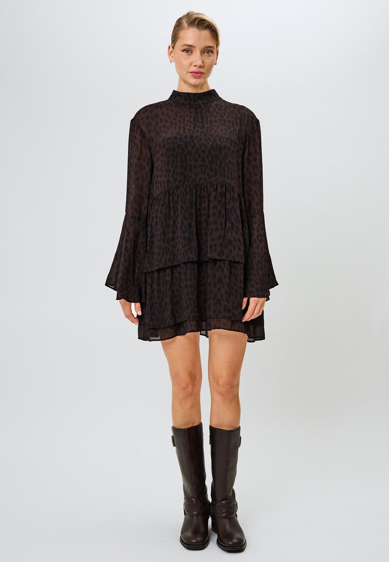 Vestido negro fluido con un diseño en capas, que presenta un estampado de leopardo y mangas de campana. Combinado con botas marrones hasta la rodilla.