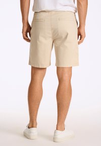Shorts beige en tissu léger, avec deux poches arrière et une coupe décontractée. L'ourlet est agrémenté d'une couture soignée.