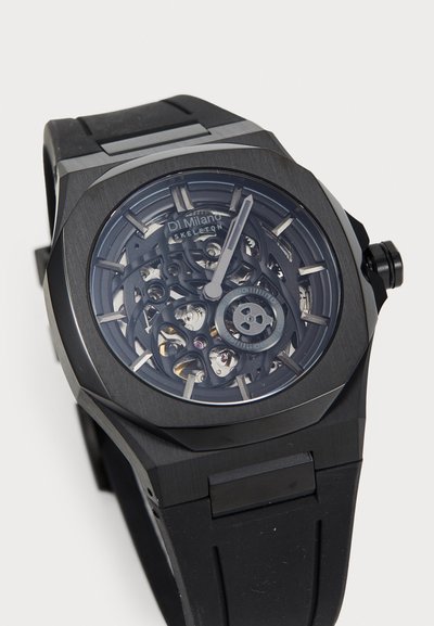 Black skeleton watch with a transparent dial revealing intricate mechanisms. Features a textured black rubber strap and angular case design.