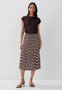 Top nero a girocollo abbinato a una gonna midi plissettata con motivo geometrico rosso e crema. Il modello indossa sandali neri con stivaletti.