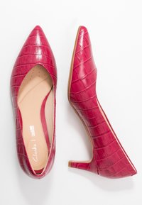 Escarpins en cuir verni rouge à bout pointu avec une texture crocodile, une semelle intérieure rembourrée et un talon fin. Logo Clarks blanc visible à l'intérieur.
