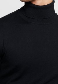 Schwarzer Rollkragenpullover aus geripptem Strickstoff. Verfügt über ein schlankes Design und einen hohen Kragen, was für ein strukturiertes Erscheinungsbild sorgt.