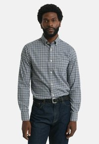 Camisa de cuadro azul y blanco con cuello, de manga larga, combinada con unos vaqueros de denim oscuros y un cinturón negro trenzado.