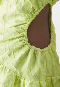 Robe vert citron avec un tissu texturé floral, des bords froncés et une découpe latérale ouverte, mettant en valeur des couches froncées et des coutures uniques.