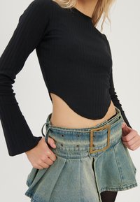 Schwarzes, geripptes Langarmoberteil, kombiniert mit einem hochgeschnittenen, hellblauen Jeansrock mit breitem Gürtel und plissierter Optik.