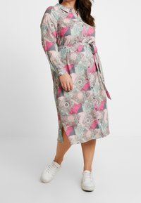 Robe à manches longues avec boutons, présentant un design en patchwork dans des teintes de rose, gris et vert. Comprend une ceinture à la taille et des fentes sur les côtés, fabriquée en tissu léger.