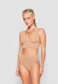 Kreminė sportinė liemenėlė su giliu V iškirpimu ir elastinga juosta, turi subtilų logotipą. Aukšto liemens bikini apatiniai puikiai dera prie komplekto. Lygi, elastinga medžiaga.