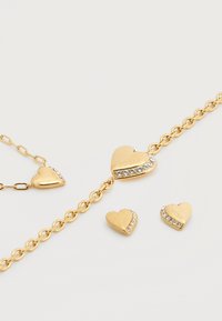 Βραχιόλι με χρυσή αλυσίδα και καρδιές-γάντζους, με διαυγείς τσιπς ρινόστοουν και χαραγμένο κείμενο. Ομοιόμορφη, λεία υφή στην επιφάνεια.