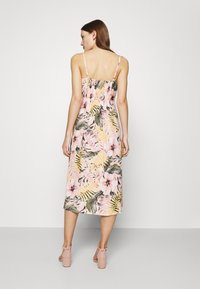 Blumen-Midi-Kleid mit pinkem Hintergrund, grünen Blättern und gelben Akzenten. Mit Spaghettiträgern und einem geschmückten Rückenteil. Kombiniert mit pinken Absatzsandalen.