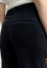 Pantaloni in corduroy neri con una texture liscia, dotati di una tasca posteriore e vita di altezza media, mostrati da un angolo laterale.