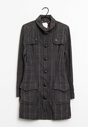 Manteau long à carreaux gris foncé avec six boutons noirs, col haut et quatre poches à rabat, suspendu à un cintre noir sur un fond blanc.
