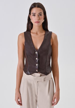 Gilet in pelle marrone con scollatura a V profonda, caratterizzato da cinque bottoni e un design aderente. Indossato sopra pantaloni beige con una vita strutturata.