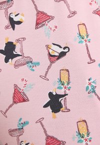 Una tela con estampado presenta pingüinos en blanco y negro, cócteles rosas y elementos festivos como vegetación y velas sobre un fondo rosa claro.