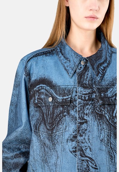 Giacca in denim con un design grafico blu e nero, collo classico, tasche frontali e dettagli in metallo argentato.