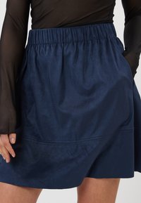 Jupe bleu marine en tissu lisse avec une ceinture élastique et des poches latérales. Présente un design minimaliste avec des détails de couture subtils.