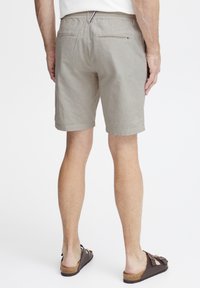 Lys beige stripete shorts med avslappet passform, elastisk midje, baklommer og oppbrettede ermer; kombinert med brune slip-on sko.