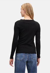 Zwarte lange mouwen top met een golvende halslijn en zoom, gemaakt van een zachte stof. Gecombineerd met hoog opgesneden blauwe denim jeans.