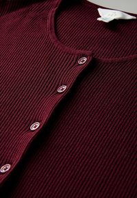 Cardigan a costine color bordeaux con scollatura rotonda e sei bottoni. Il tessuto ha una superficie texturizzata e presenta bottoni coordinati.